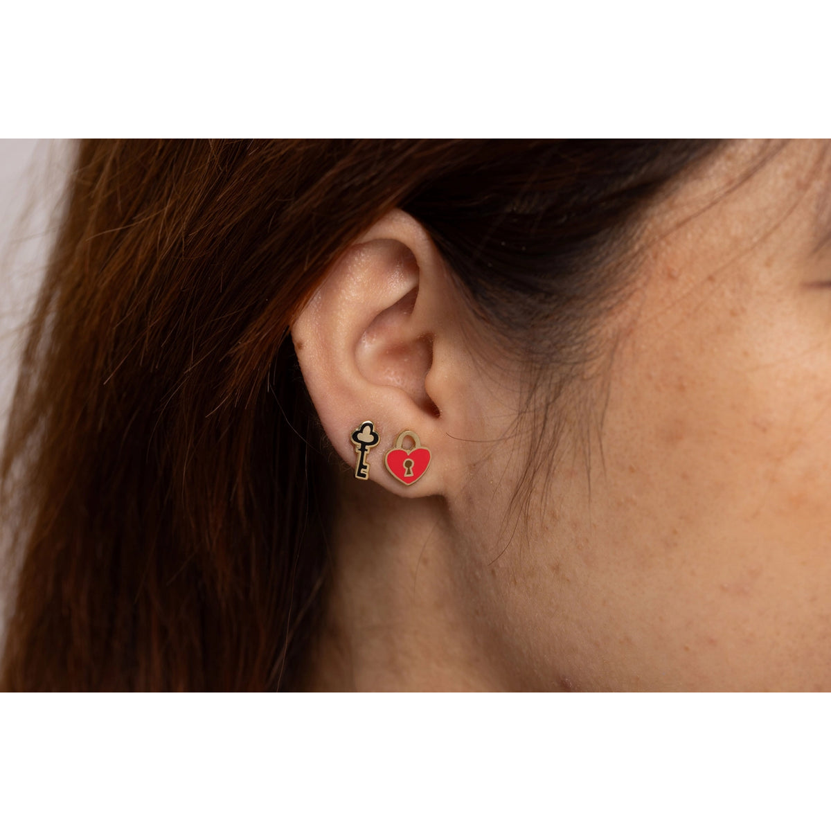 Close-up of an ear wearing a key-shaped earring with a red heart on a white background