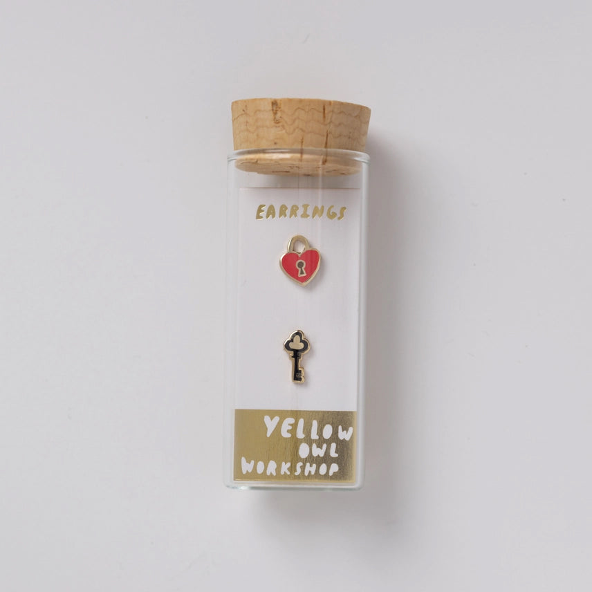 Clear container with cork lid holding earrings labeled 'Yellow Owl Workshop' on a white background
