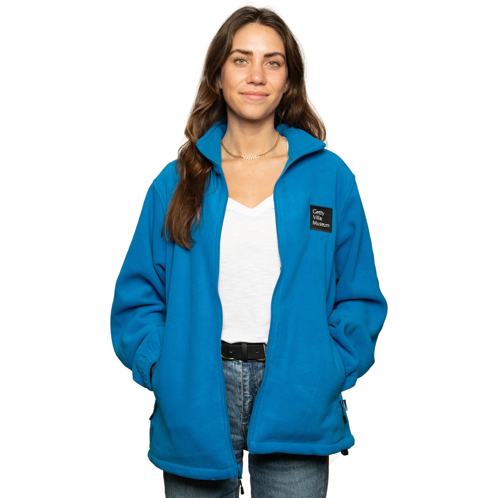 A woman wearing a blue full-zip fleece jacket with the Getty Villa Museum logo embroidered on the chest, standing against a plain background.