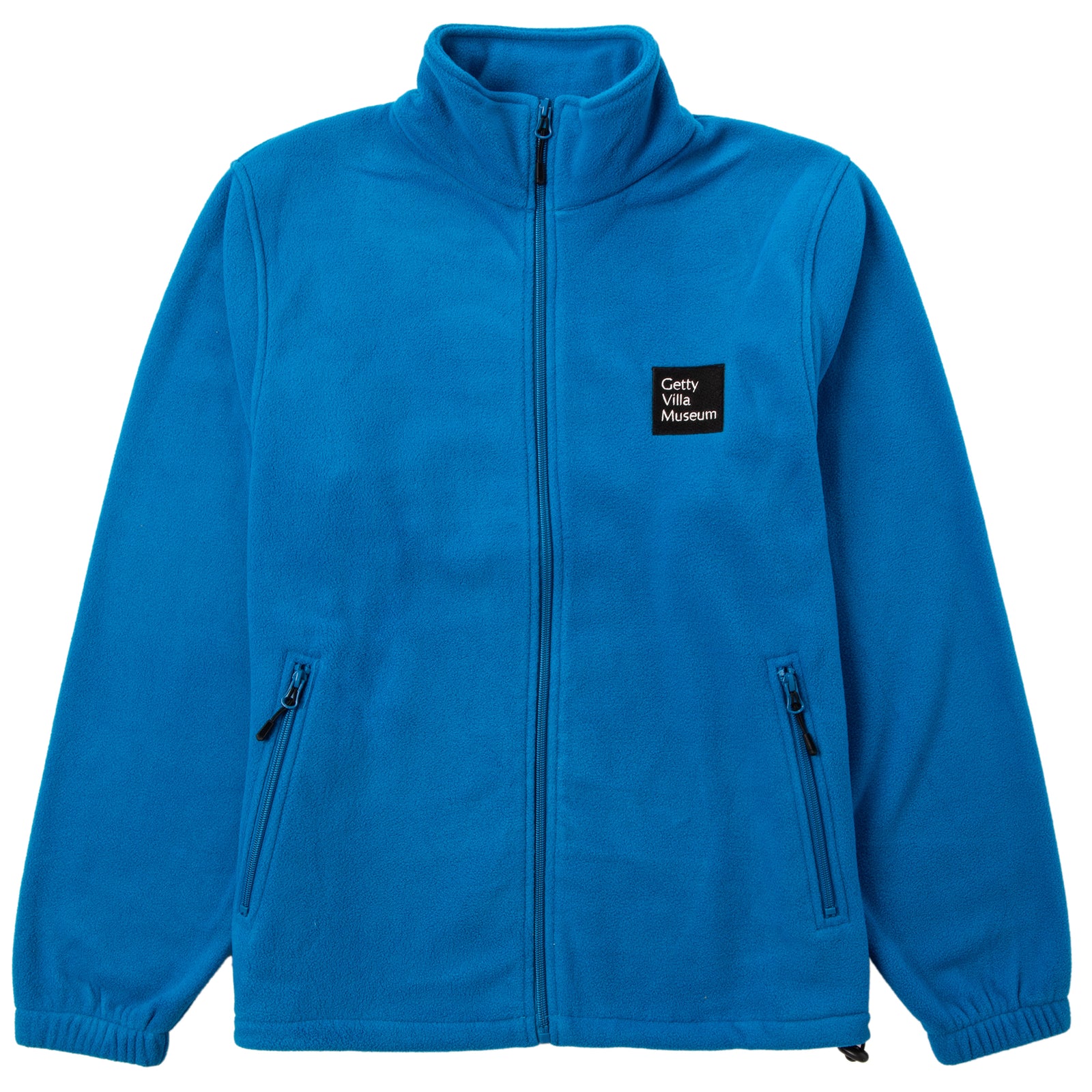 A woman wearing a blue full-zip fleece jacket with the Getty Villa Museum logo embroidered on the chest, standing against a plain background.