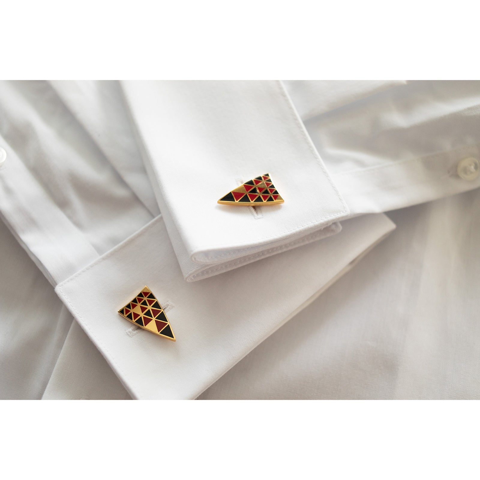 A pair of triangular cufflinks with a geometric pattern featuring gold, red, and black colors.