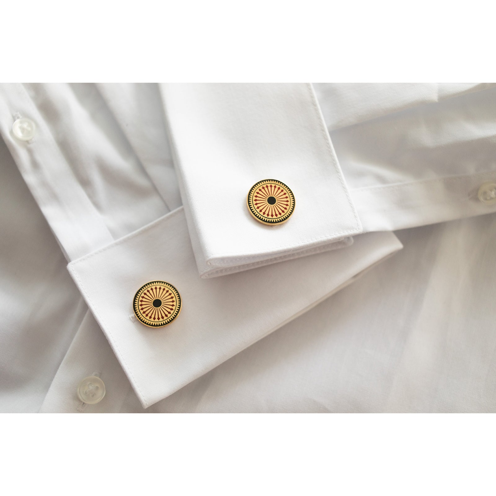 A pair of gold-colored cufflinks with a geometric pattern featuring a series of concentric circles and triangles.