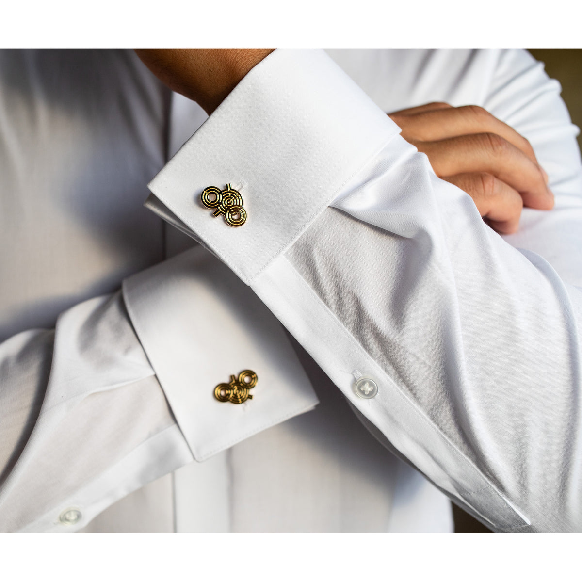 Close-up of a white shirt with gold cufflinks worn by a person.