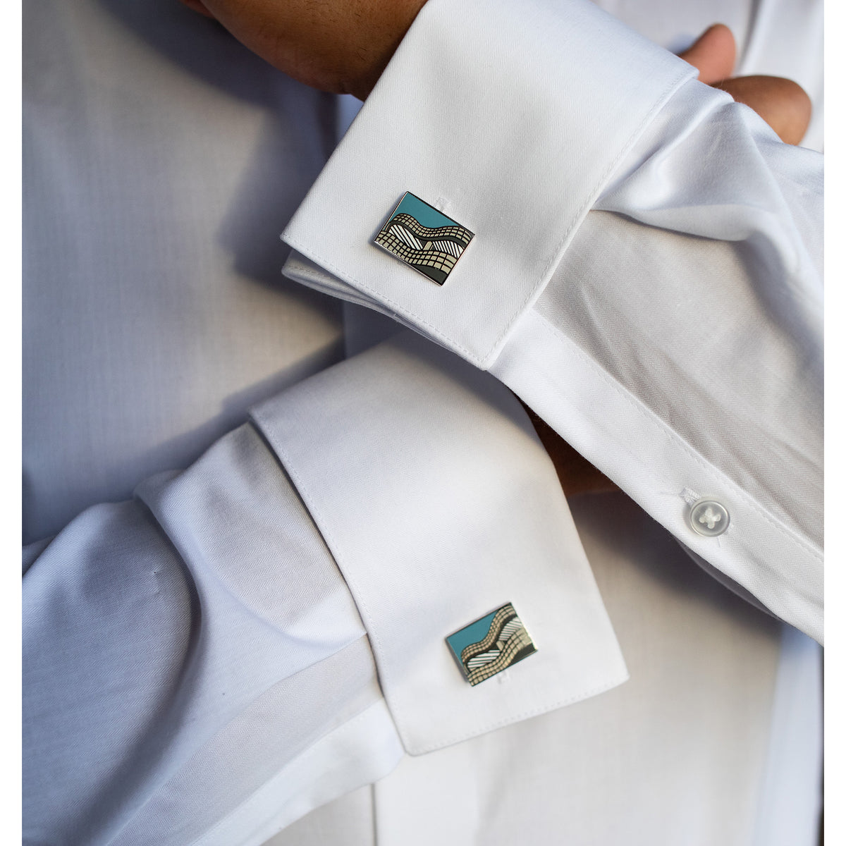 Close-up of a white shirt with cufflinks featuring geometric patterns.