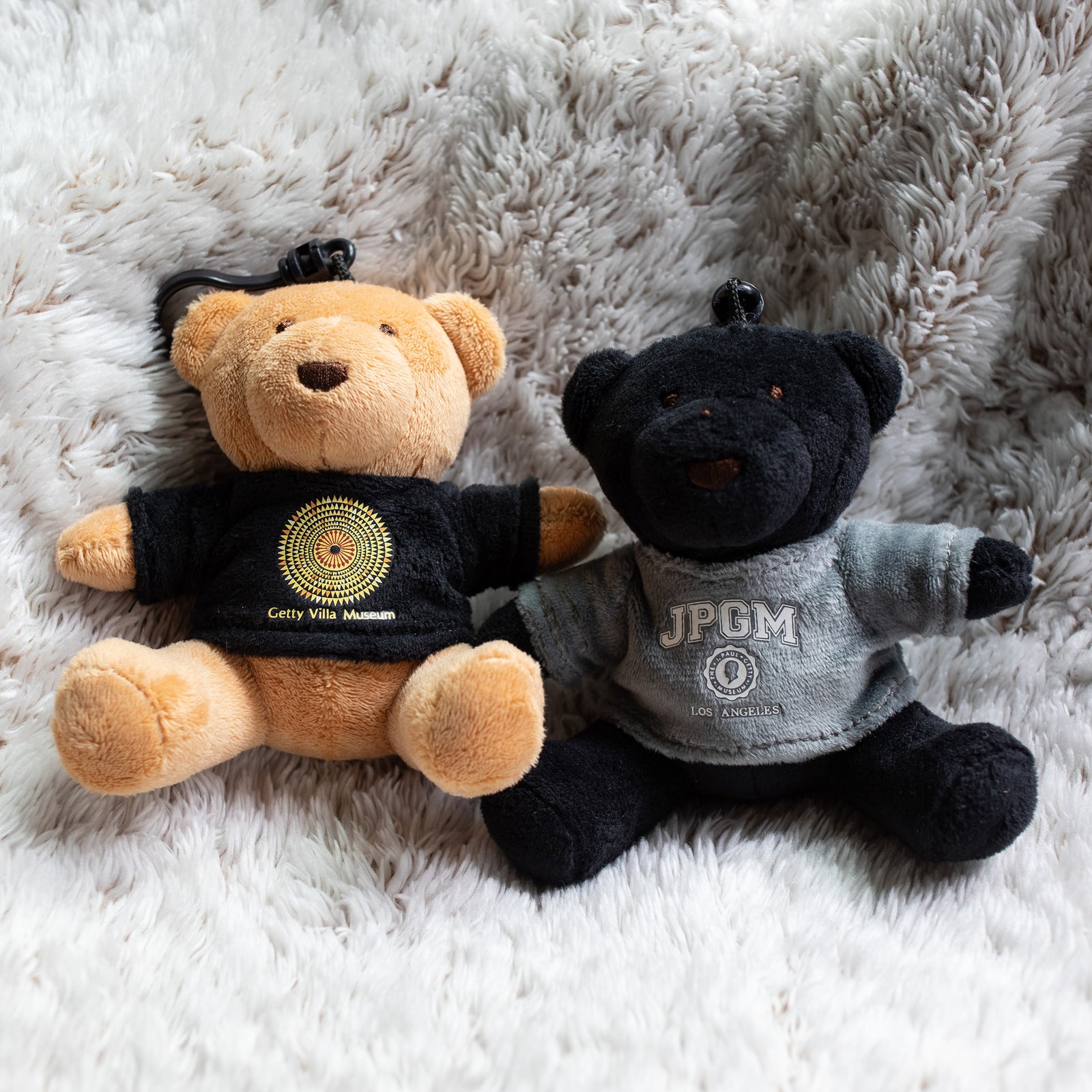 A plush black teddy bear wearing a grey sweatshirt with 'JPGM LOS ANGELES' printed on it.