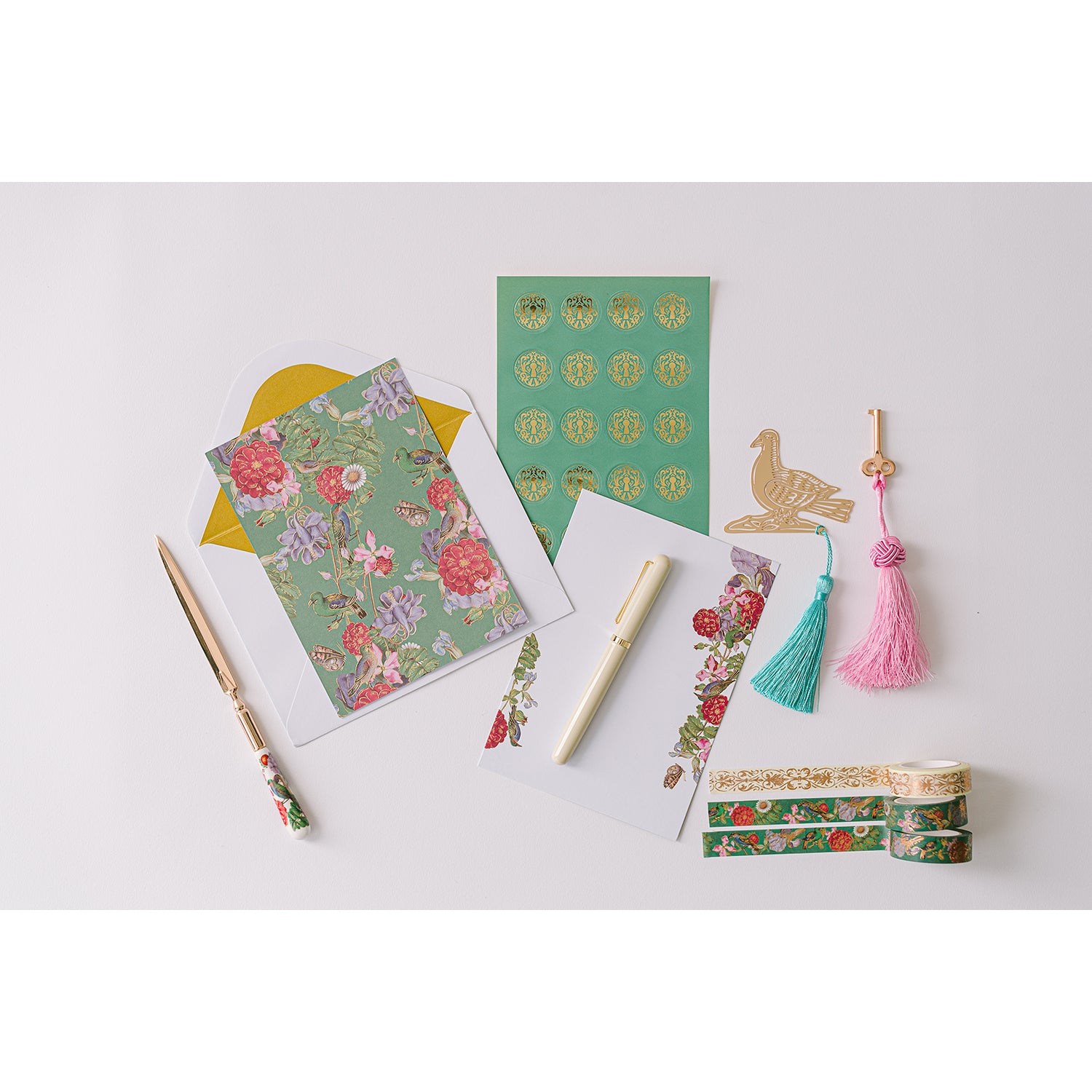 A lacquer keepsake box with a pink interior, containing stationery items including writing sheets, envelopes, stickers, bookmarks, washi tapes, a ballpoint pen, and a ceramic letter opener. The box is teal in color with a decorative tassel.