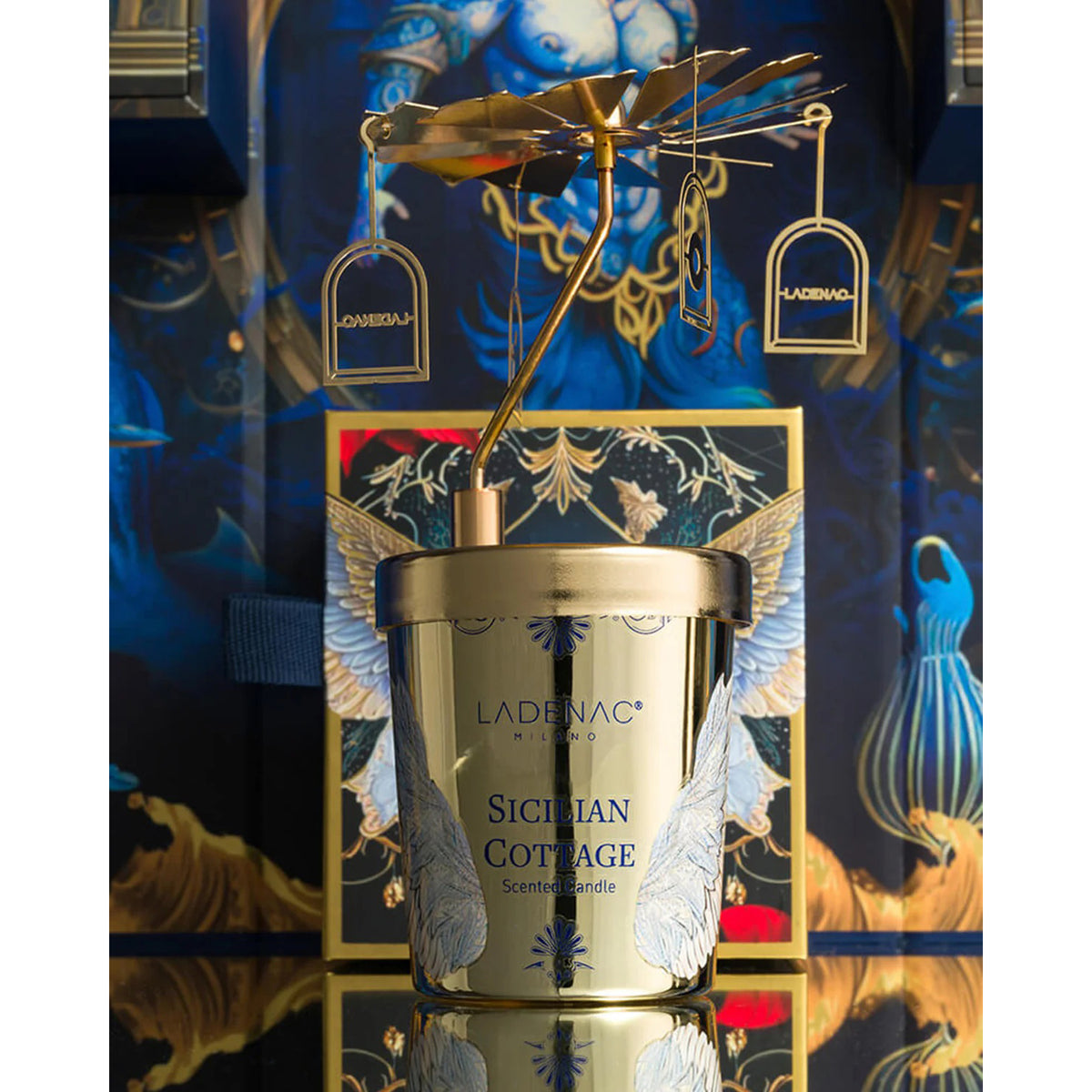 Gold candle with &#39;Ladenac&#39; branding against a decorative blue background
