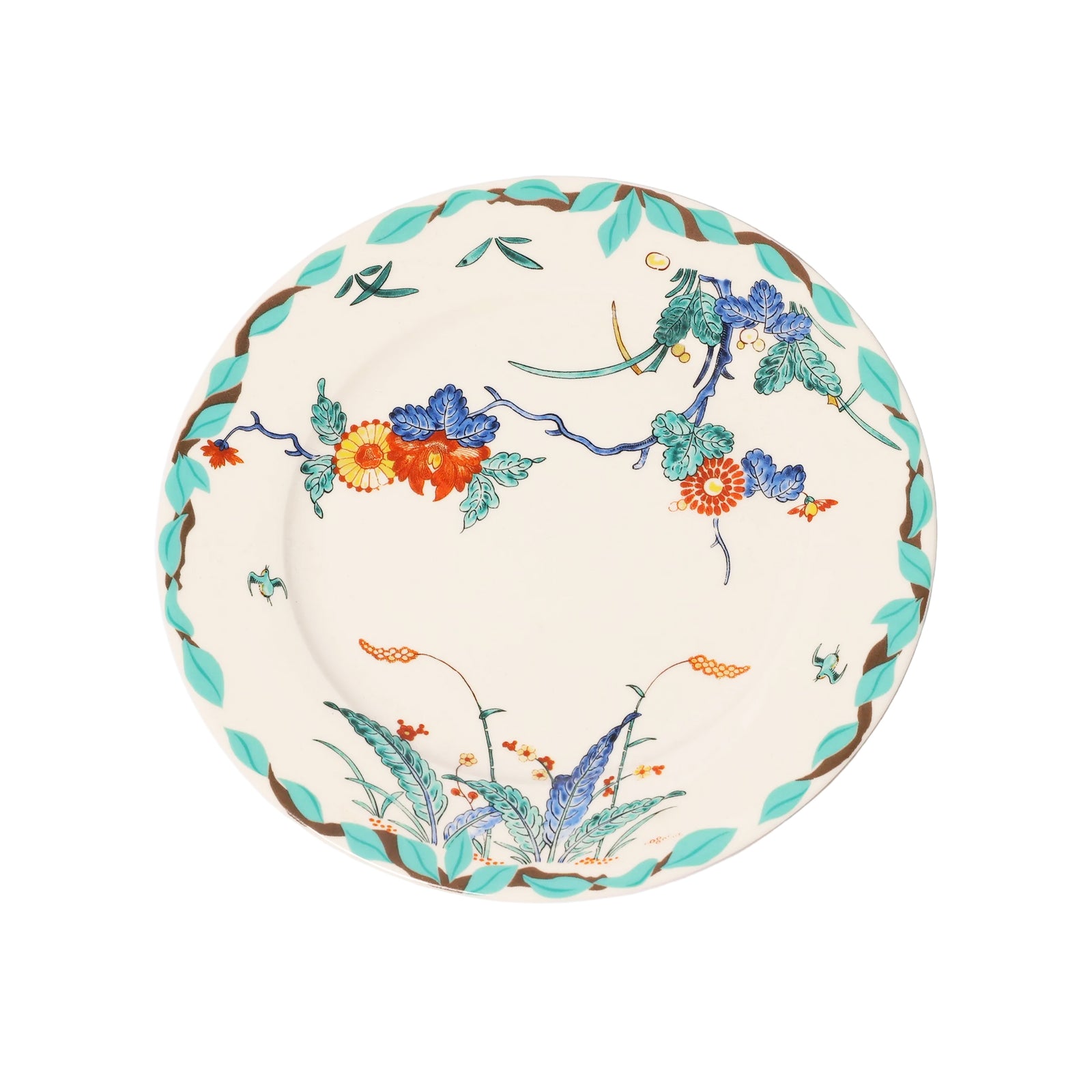 A round ceramic plate with a cream-colored glaze, decorated with a colorful floral branch pattern in blue, orange, and green, and a braided brown and turquoise border.
