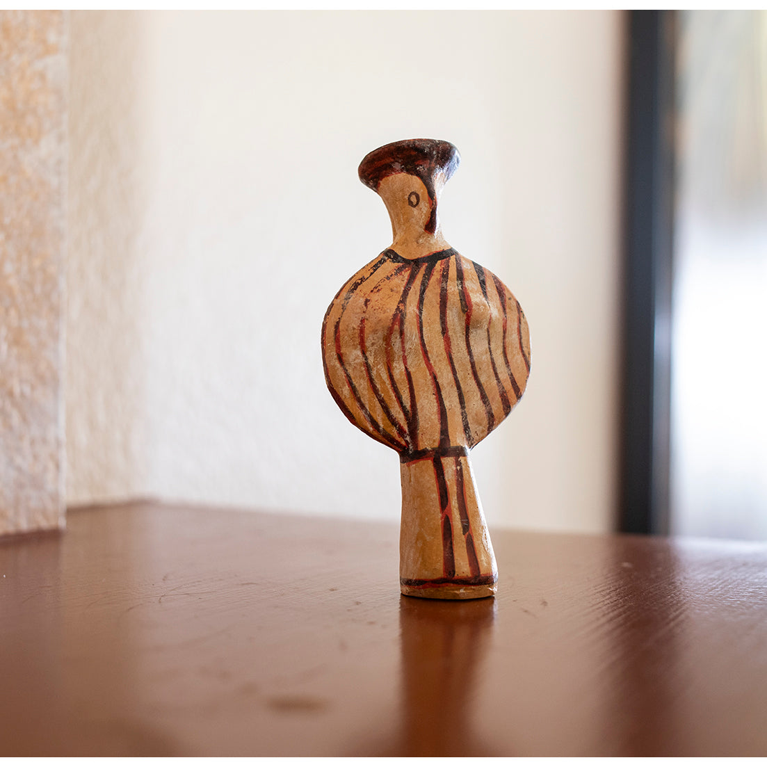 Ceramic figure with striped design on a white background on a wooden surface