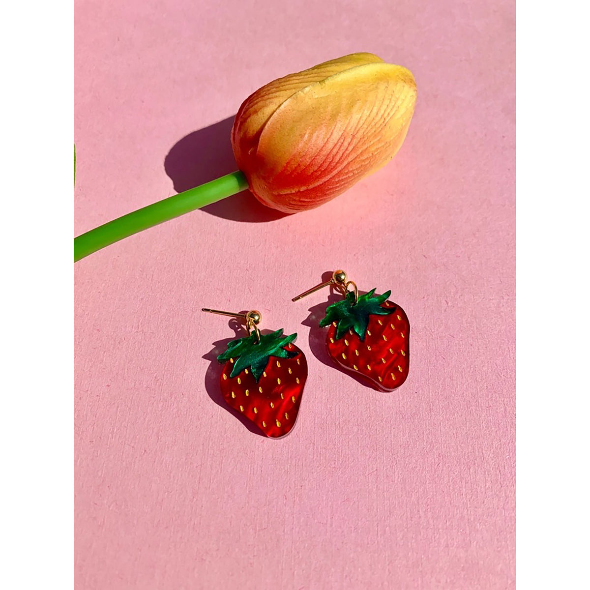 Strawberry-shaped earrings on a pink background with a tulip.