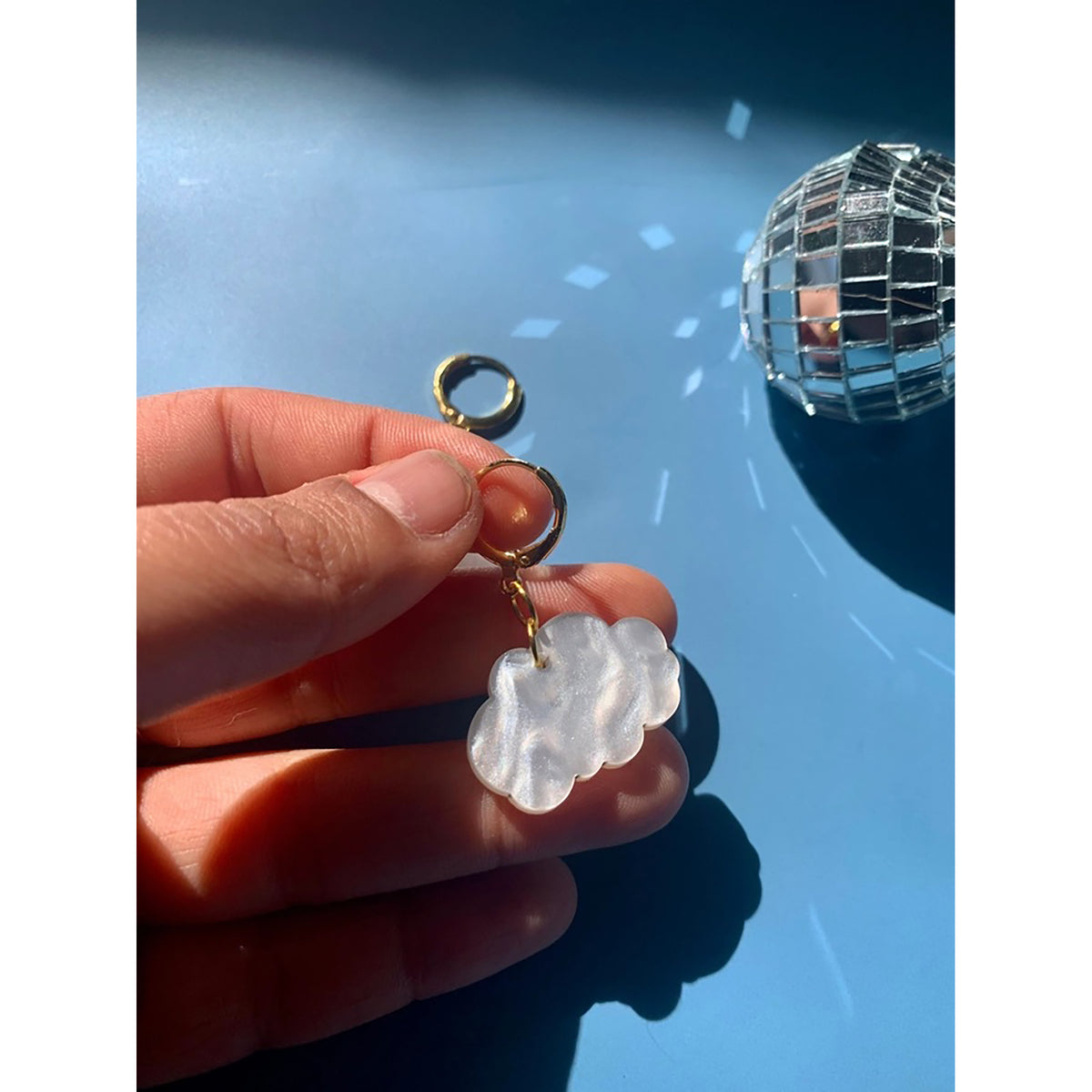 Hand holding a cloud-shaped keychain with a disco ball in the background