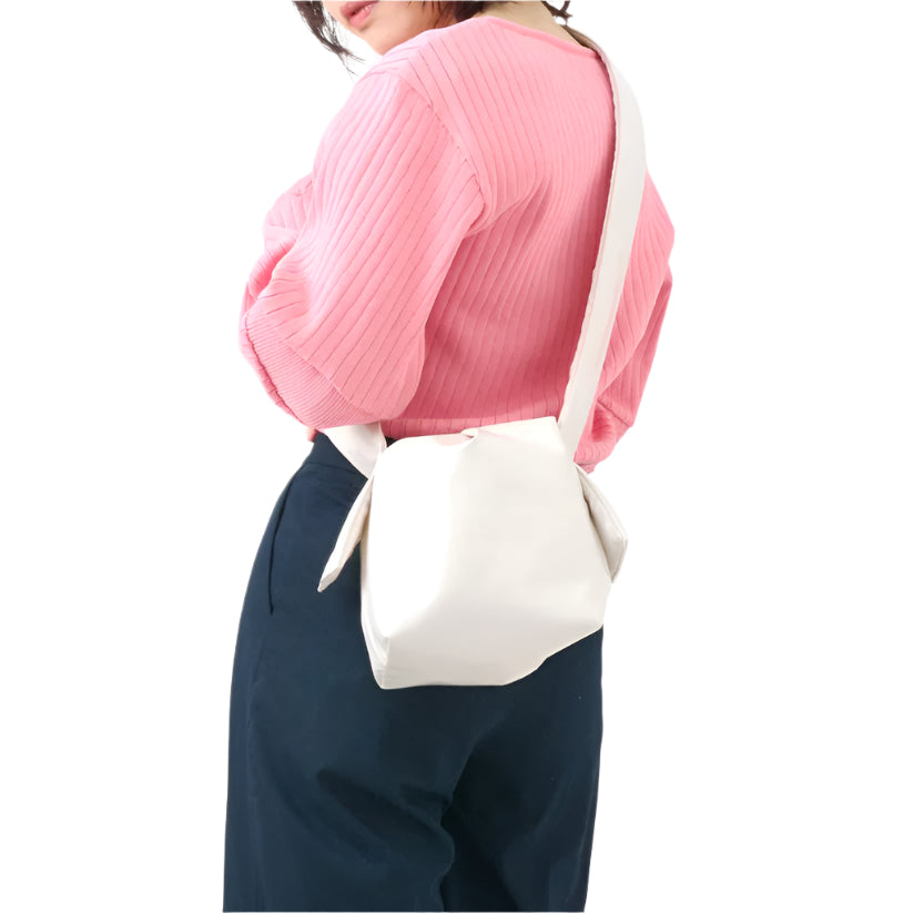 A person wearing a pink sweater and white trousers is seen from behind, carrying a white shoulder bag with a thick strap.