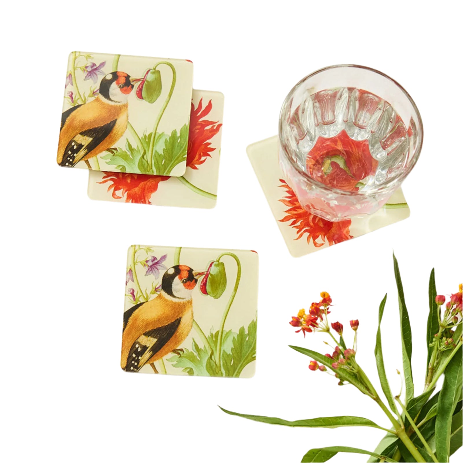 A set of four square acrylic coasters with floral and bird illustrations, intended to be used as coasters or magnets, displayed alongside a glass of red liquid and additional floral decor.