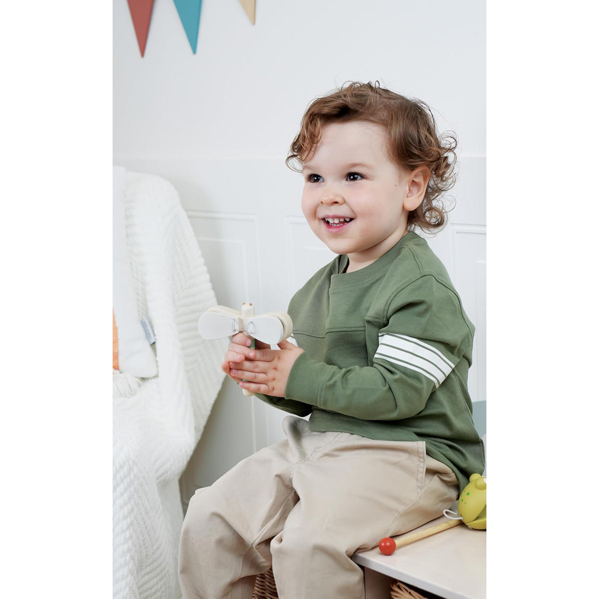 Child wearing a green sweatshirt with white stripes sitting on a chair.