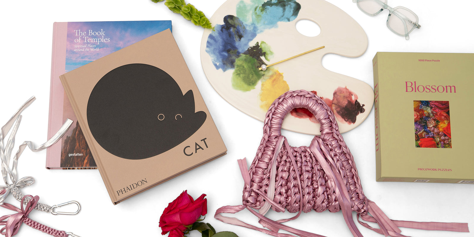 Pink woven bag, books, and paint palette on a white background