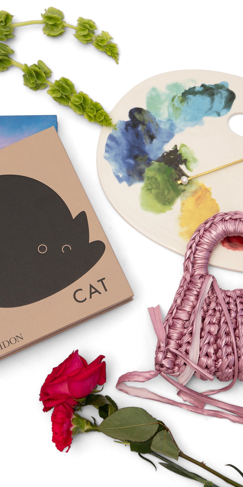 Cat-themed book, floral palette, pink woven bag, and red rose on a white background