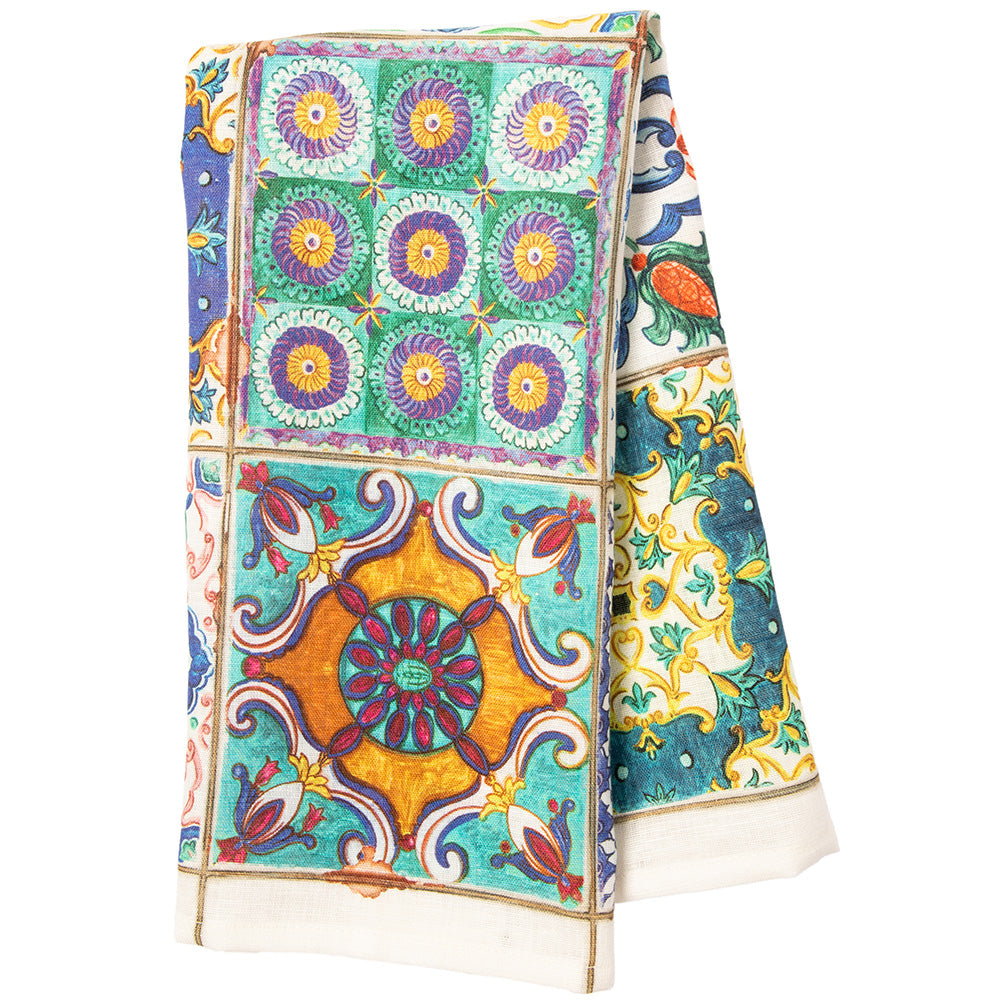 A tea towel featuring a collection of square Italian tiles with various floral and geometric patterns in a variety of colors including blue, green, yellow, and white.