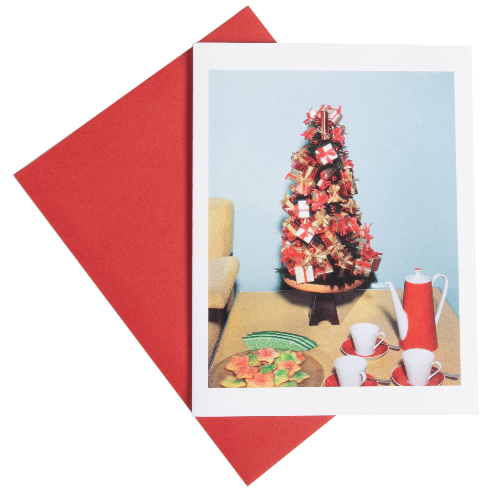 A holiday greeting card featuring a photograph of a Christmas tree, presents, and a red and white coffee set, with a red envelope.