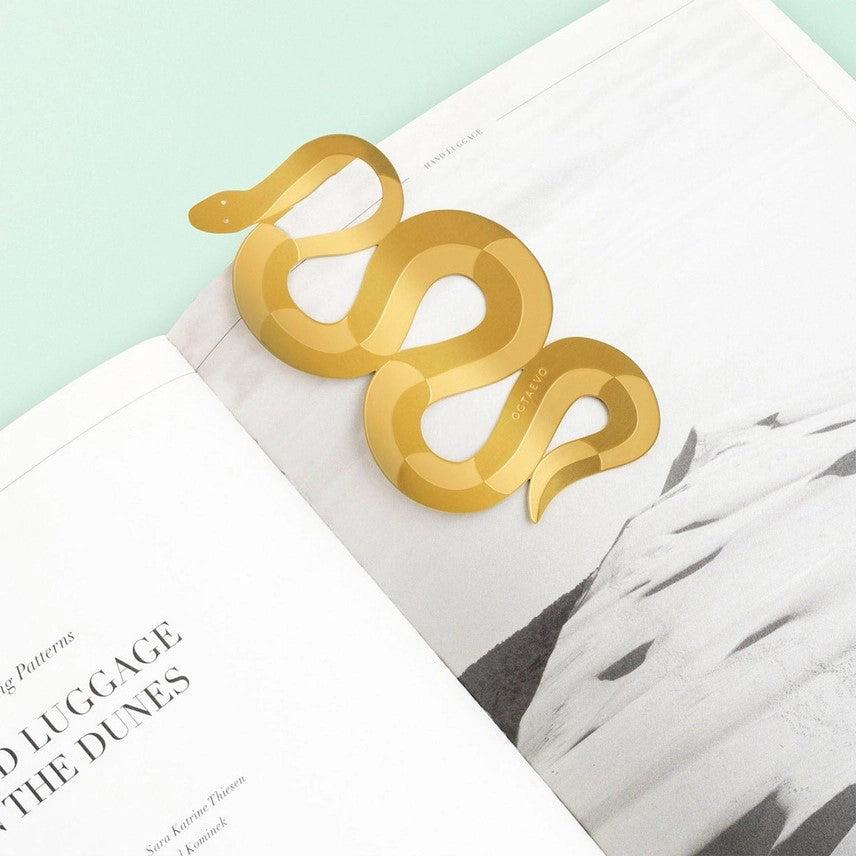 A brass bookmark designed in the shape of a coiled snake, presented on a card