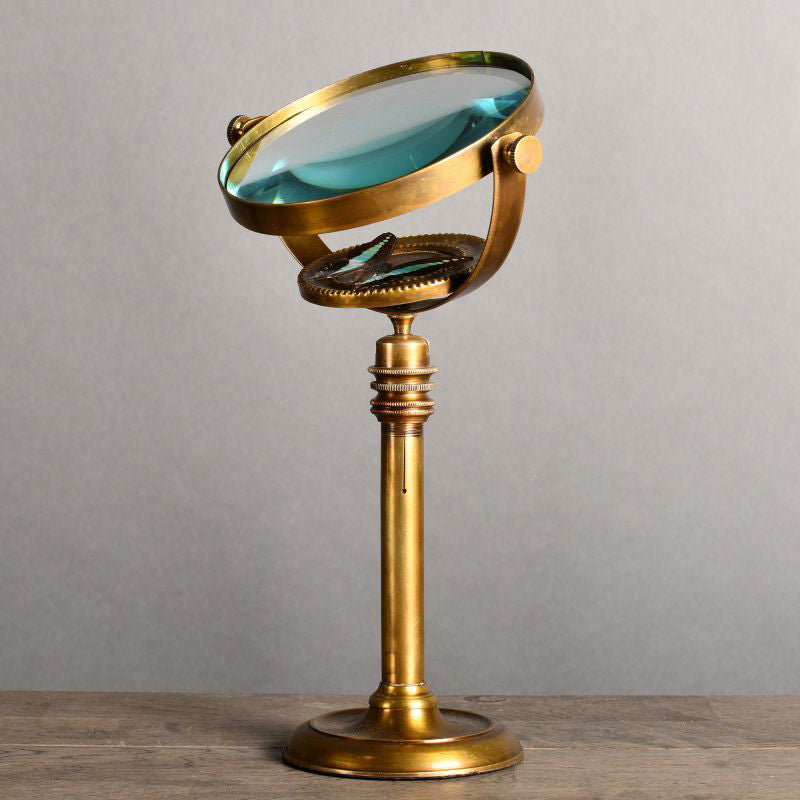 A 19th-century style entomologist's magnifying glass with a brass and glass construction, featuring a gilded finish and a telescopic stand on a white background