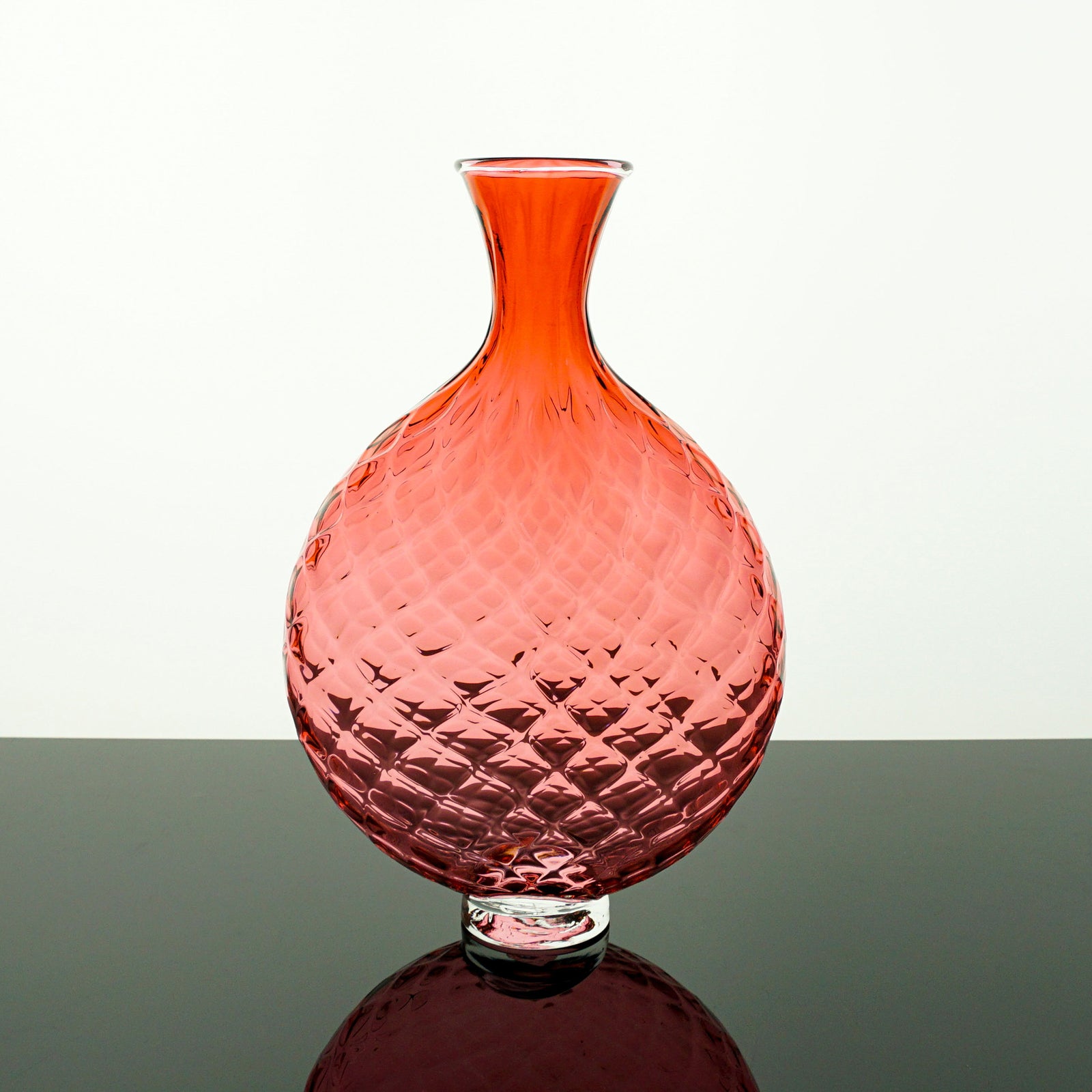 Coral-colored glass vase with textured surface on a white background