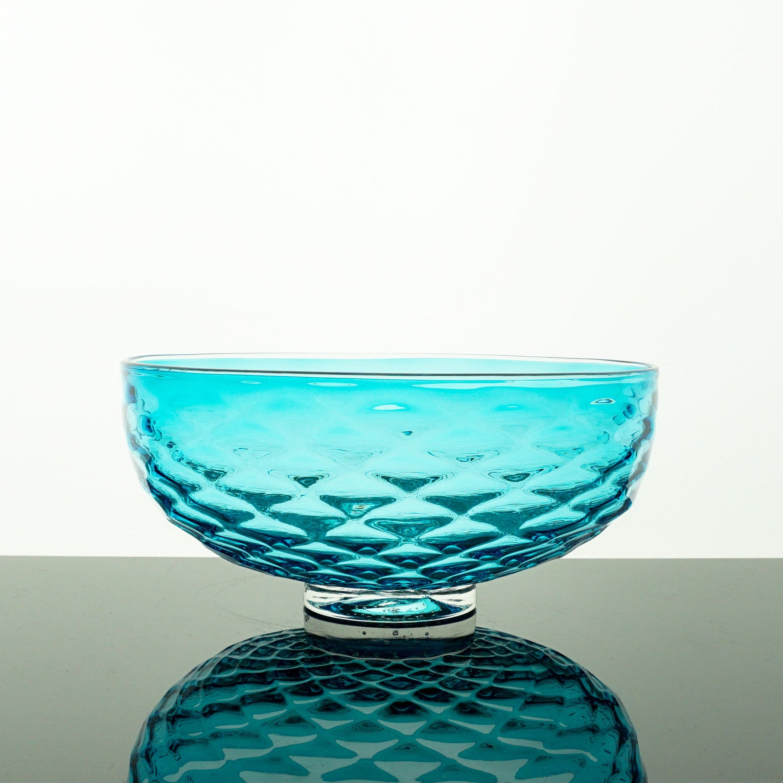 Turquoise glass bowl with textured design on a white background