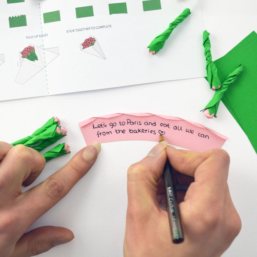 Hands writing on a pink paper with green decorative elements and printed text in the background.