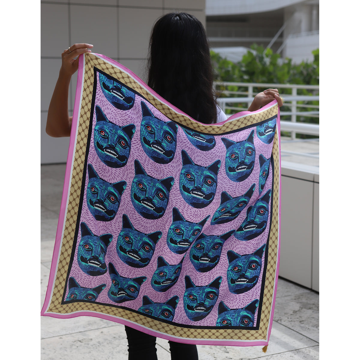 Person holding a quilt with blue cat faces on a pink background