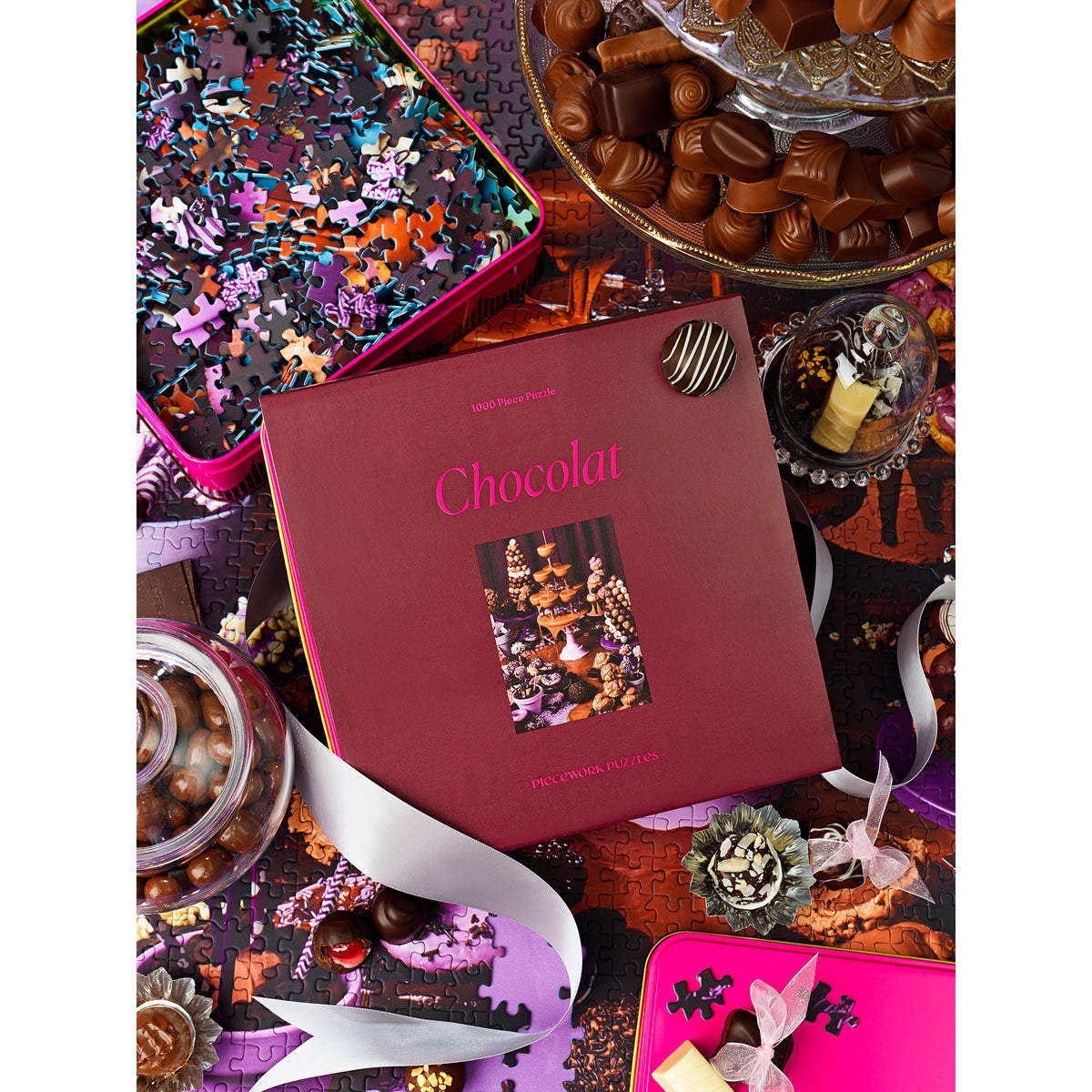 Maroon chocolate box with 'Chocolat' text surrounded by various chocolates and a puzzle