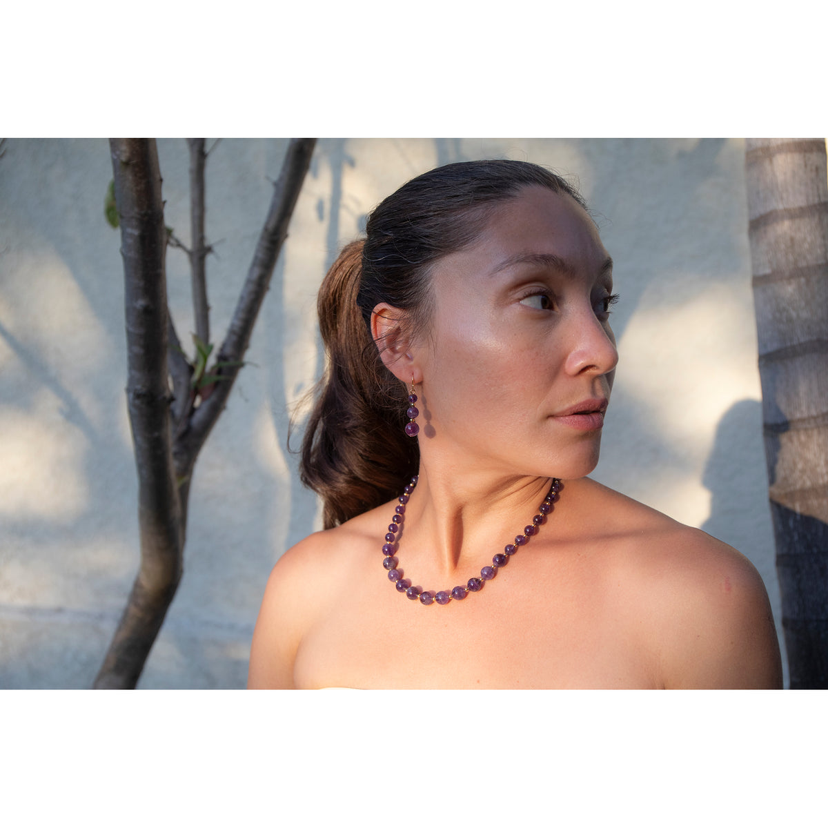 Woman wearing a purple beaded necklace and earrings outdoors