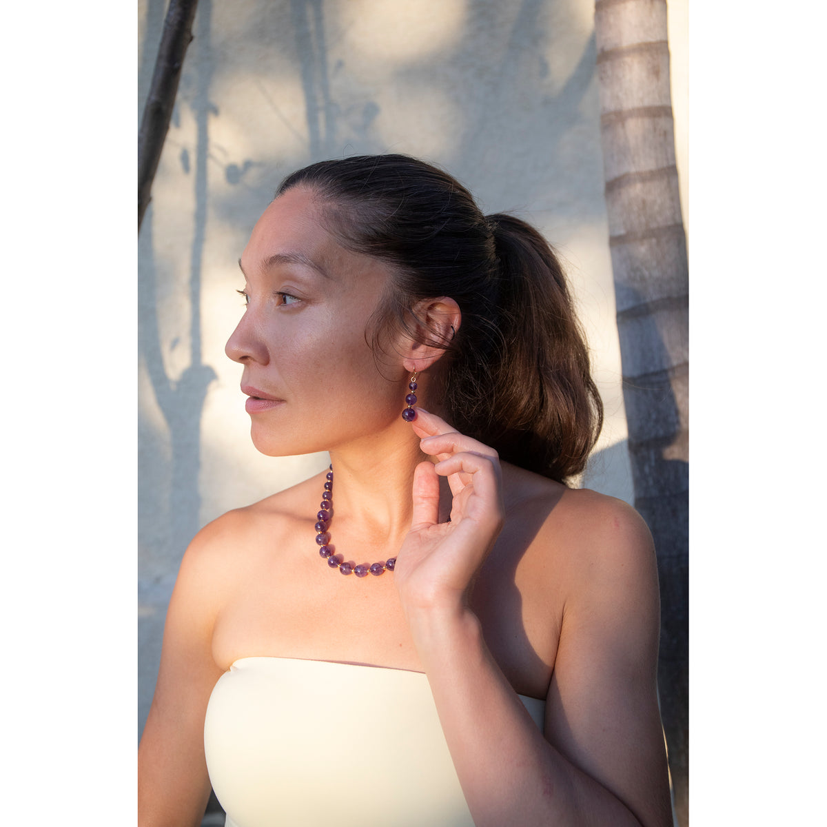 Woman wearing a necklace and earrings outdoors with palm trees in the background