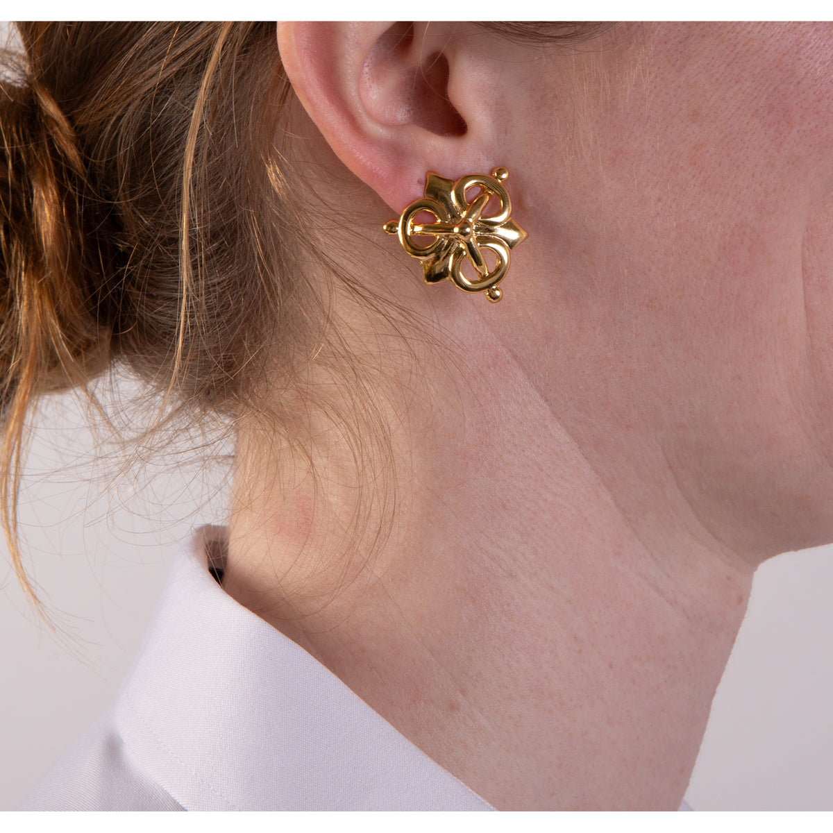 Gold floral earring worn by a person with a white shirt background