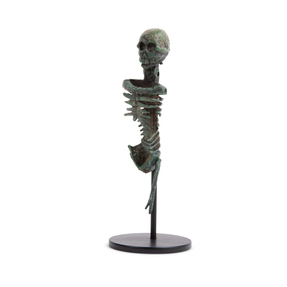 A miniature bronze skeleton with a green patina, displayed on a metal stand, representing a historical reproduction.