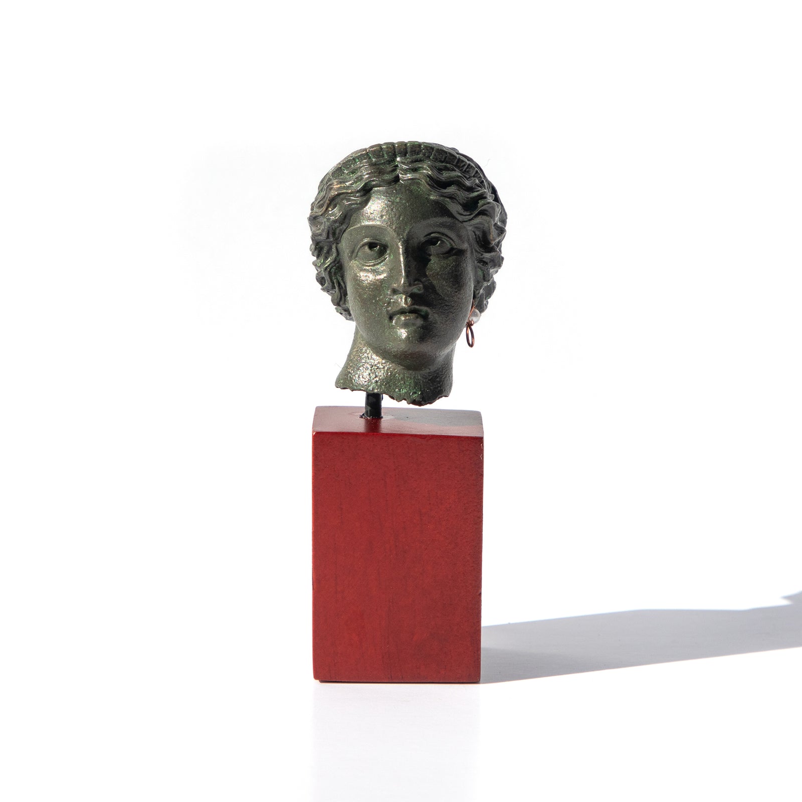 A sculpture reproduction of the Head of Venus with Pearl Earring, placed on a red base, with a greenish tint representing the age-old material.
