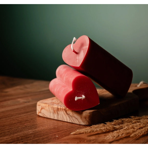 Two heart-shaped red candles on a wooden stand with a dark green background