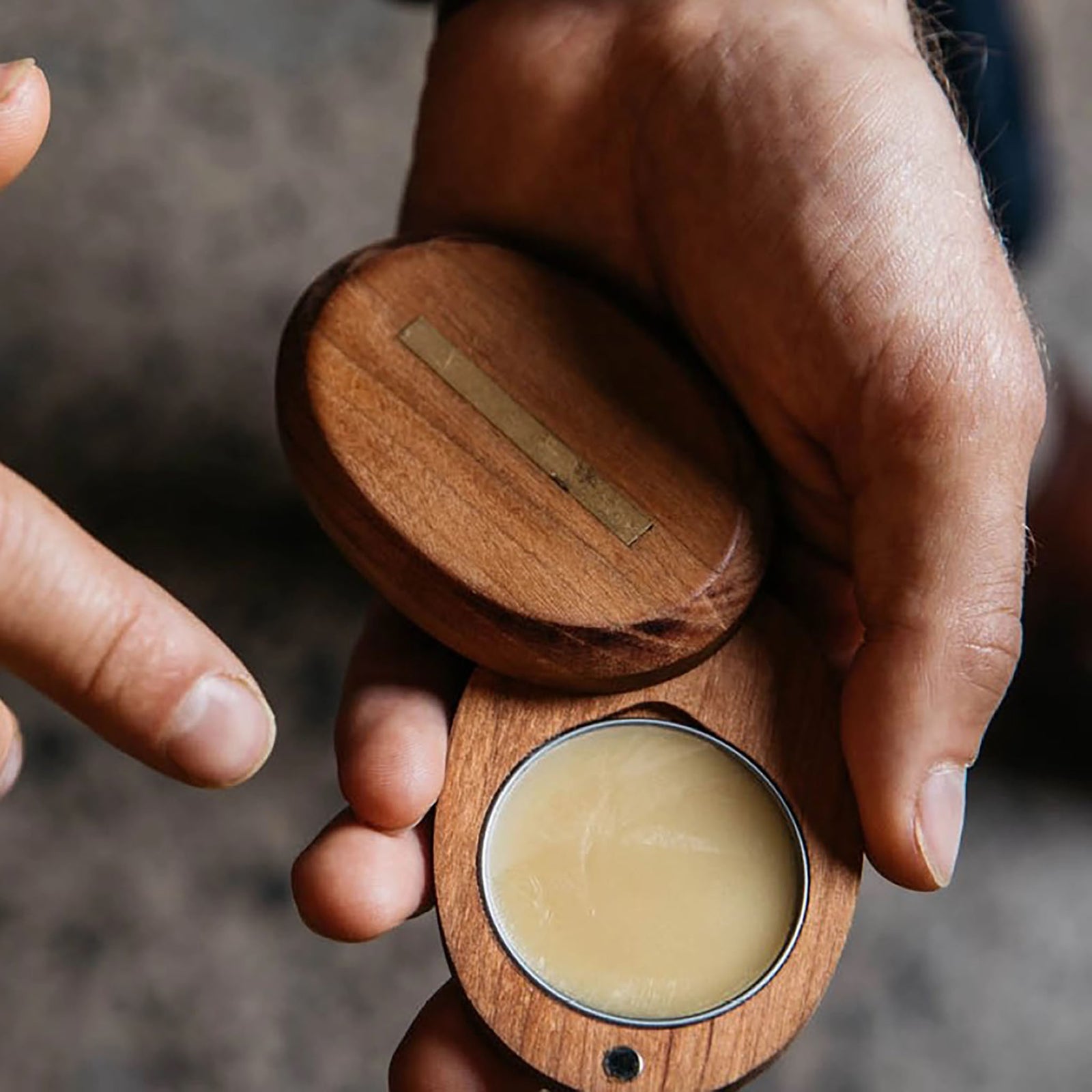 A solid cologne case with a wooden lid, labeled 'Underhill', next to its packaging box which has 'Smoke & Leather' indicated as the scent.