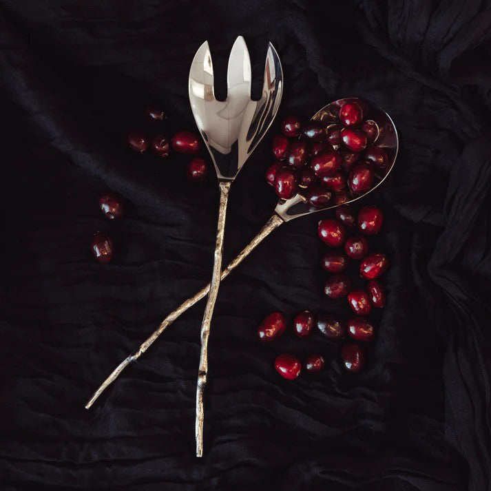 Silver salad servers with red berries on a dark textured surface