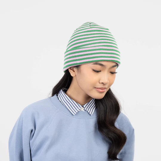 Person wearing a green and lilac striped beanie against a light gray background