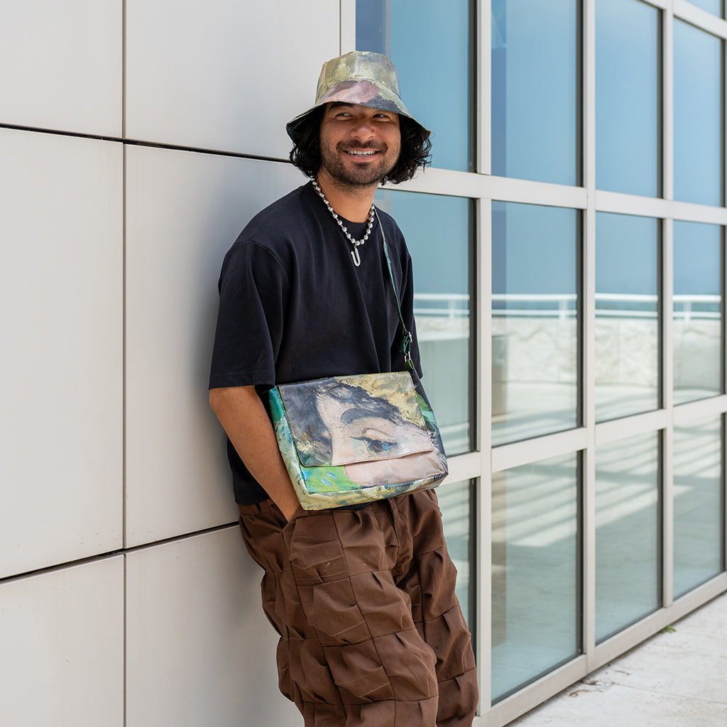 Man leaning against a wall holding a colorful bag, with a modern building in the background