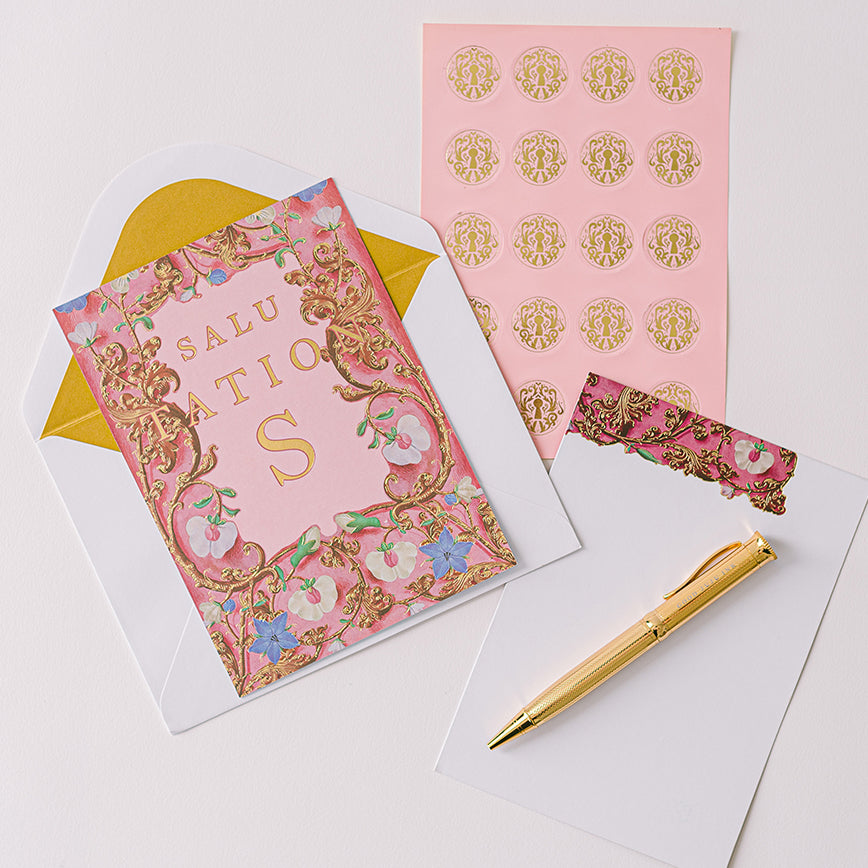 Decorative pink card with gold text, gold pen, and matching paper on a white background