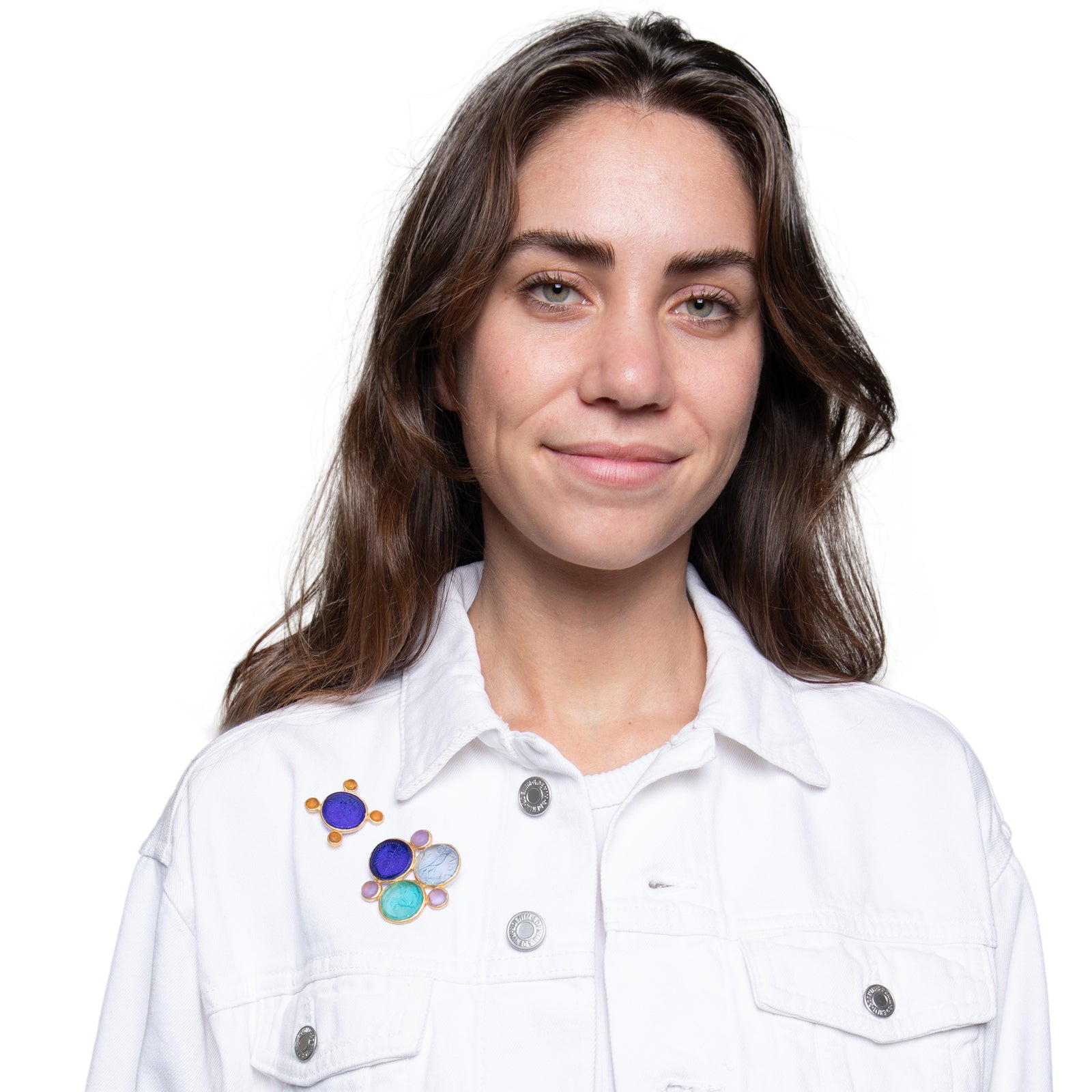 A glass multi-coin brooch with vibrant blue, green, and purple colors, featuring intricate embossed designs resembling coins, surrounded by a gold-tone metal frame.