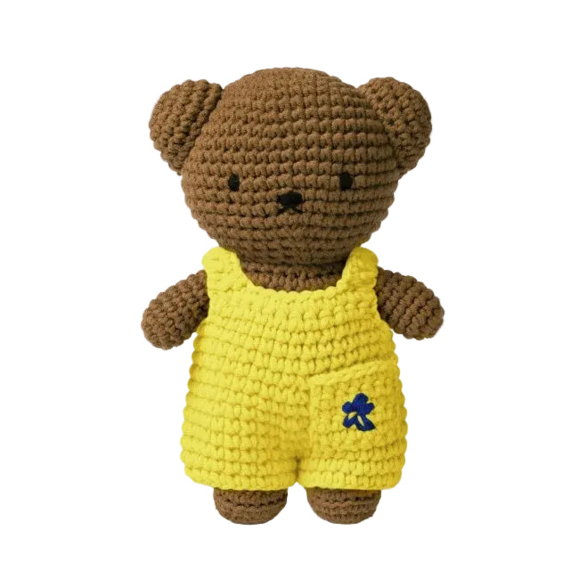 Crocheted teddy bear wearing a yellow outfit with a blue logo on a white background