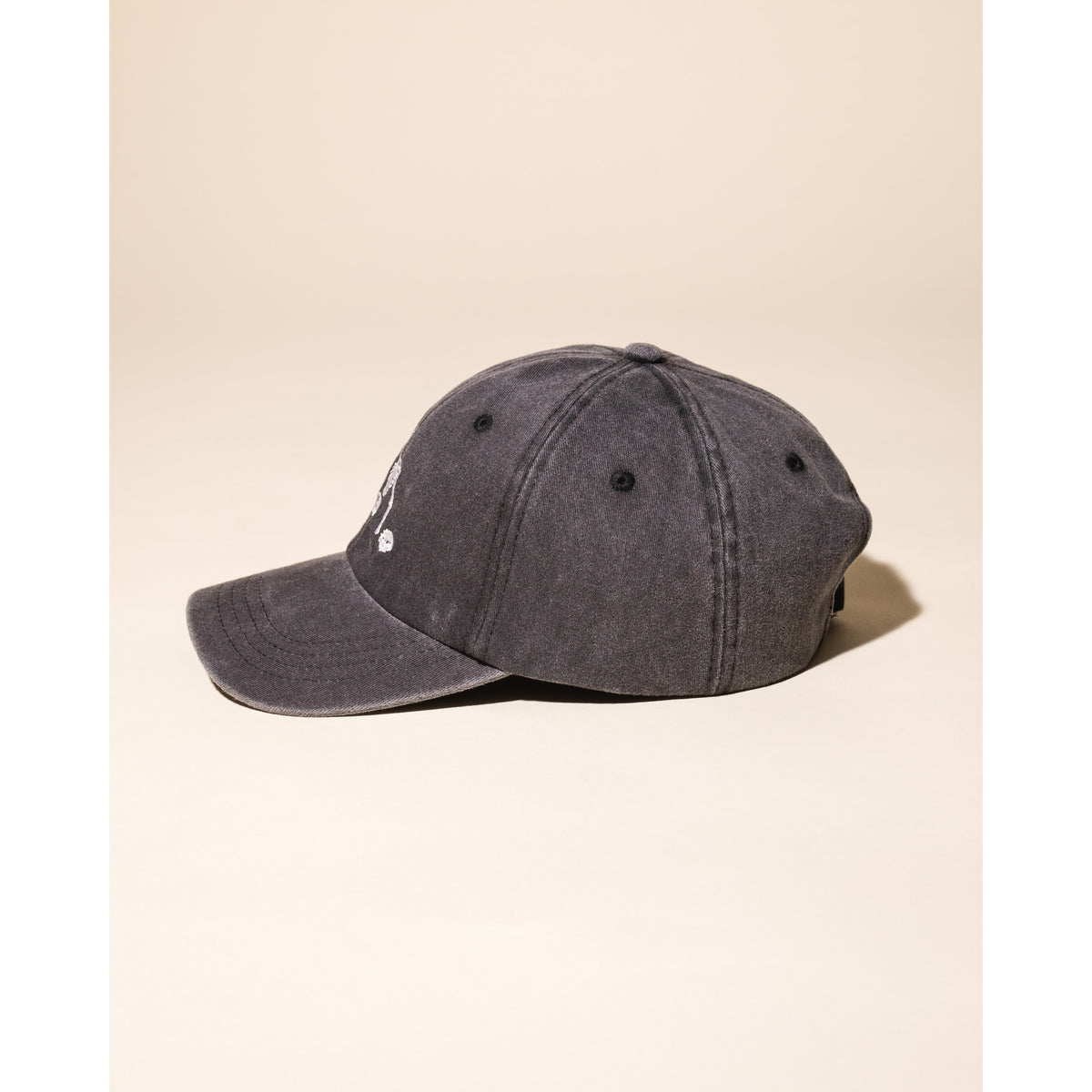 A washed charcoal gray baseball cap with a small white embroidered logo on the front, shown from a side profile against a solid beige background.