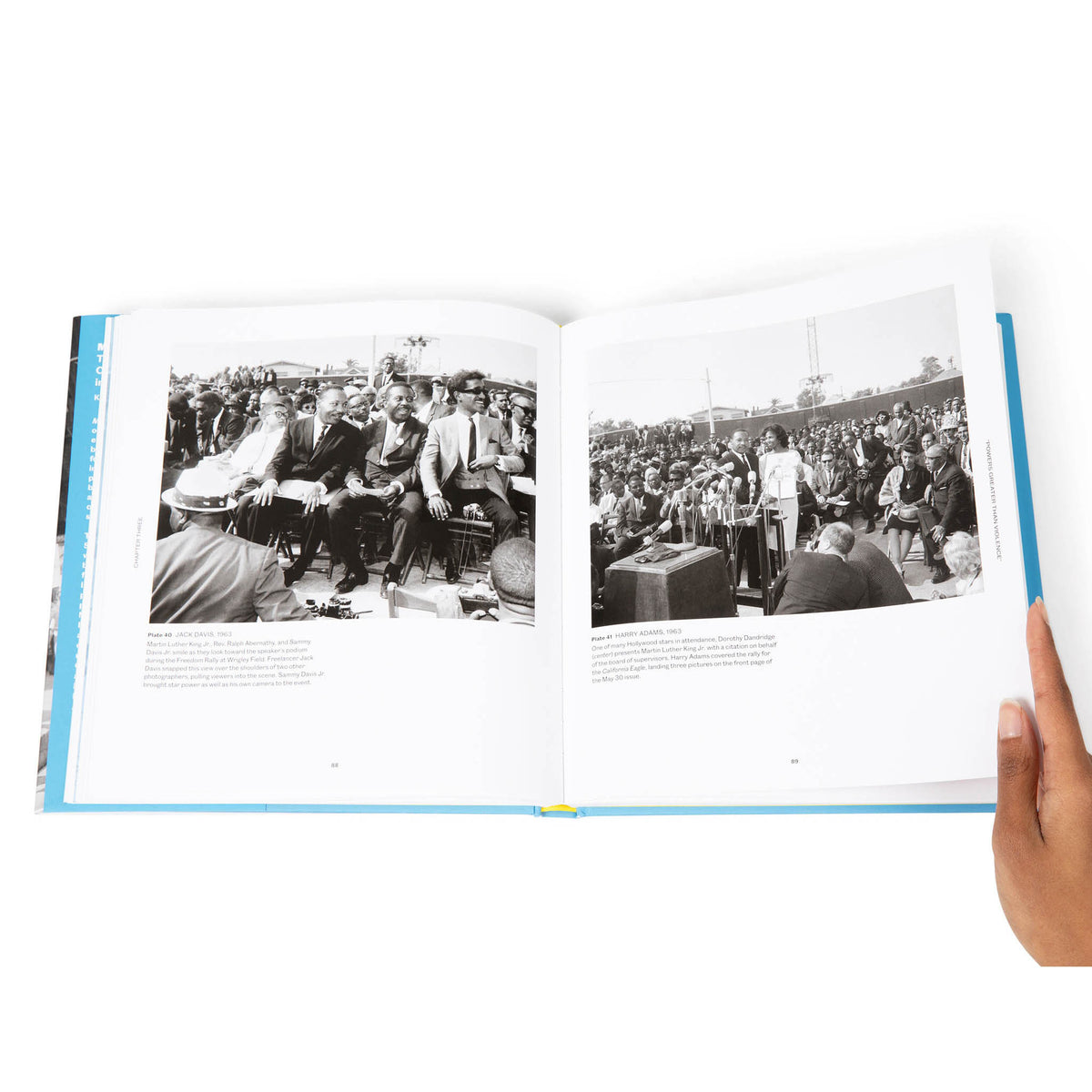Open book showing black and white photos of a crowd, held open by a hand.