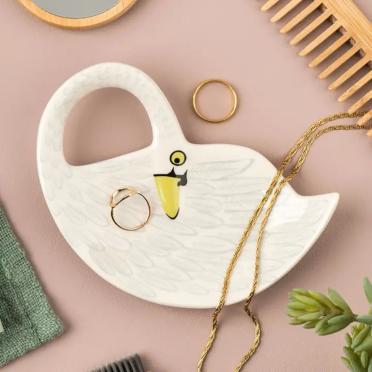 White swan-shaped dish with gold rings on a pink background