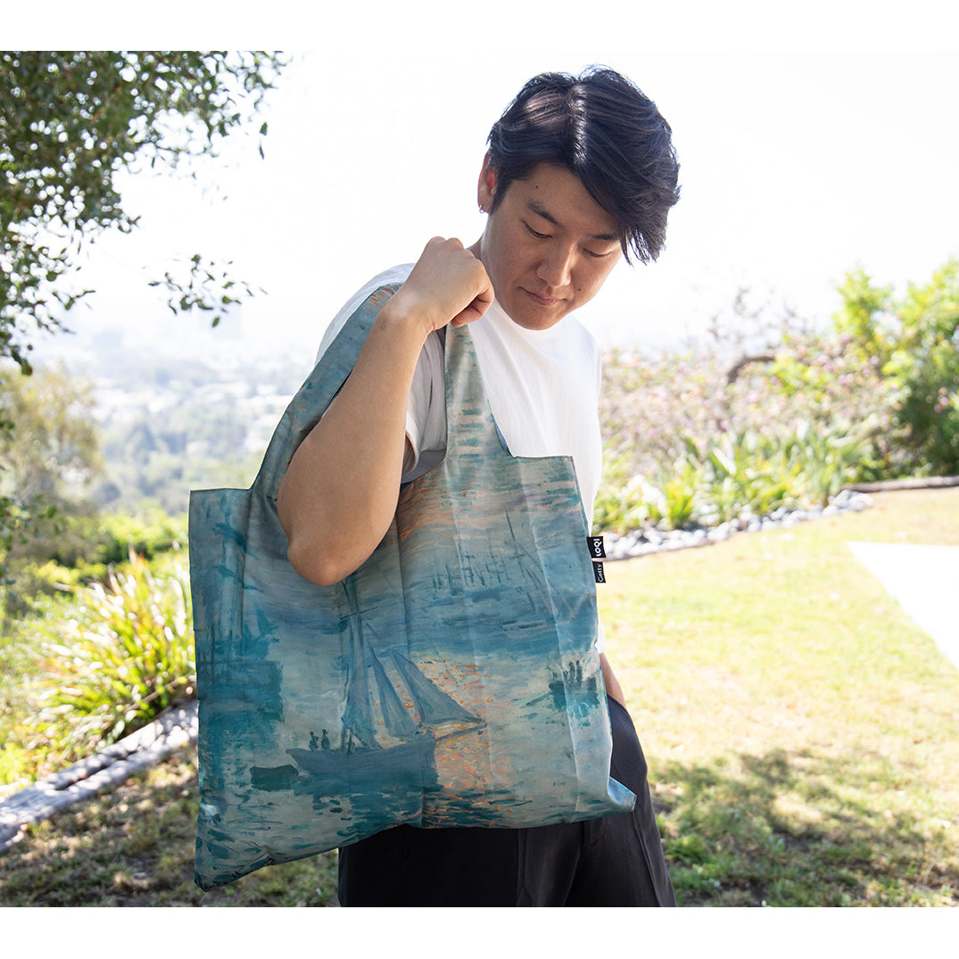 A tote bag featuring a printed image of a Monet painting with a marine scene, including boats and a sunrise sky.