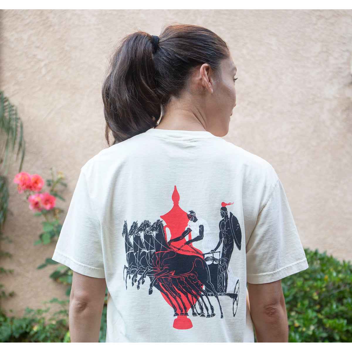 Person wearing a white t-shirt with a graphic design on the back, standing outdoors.