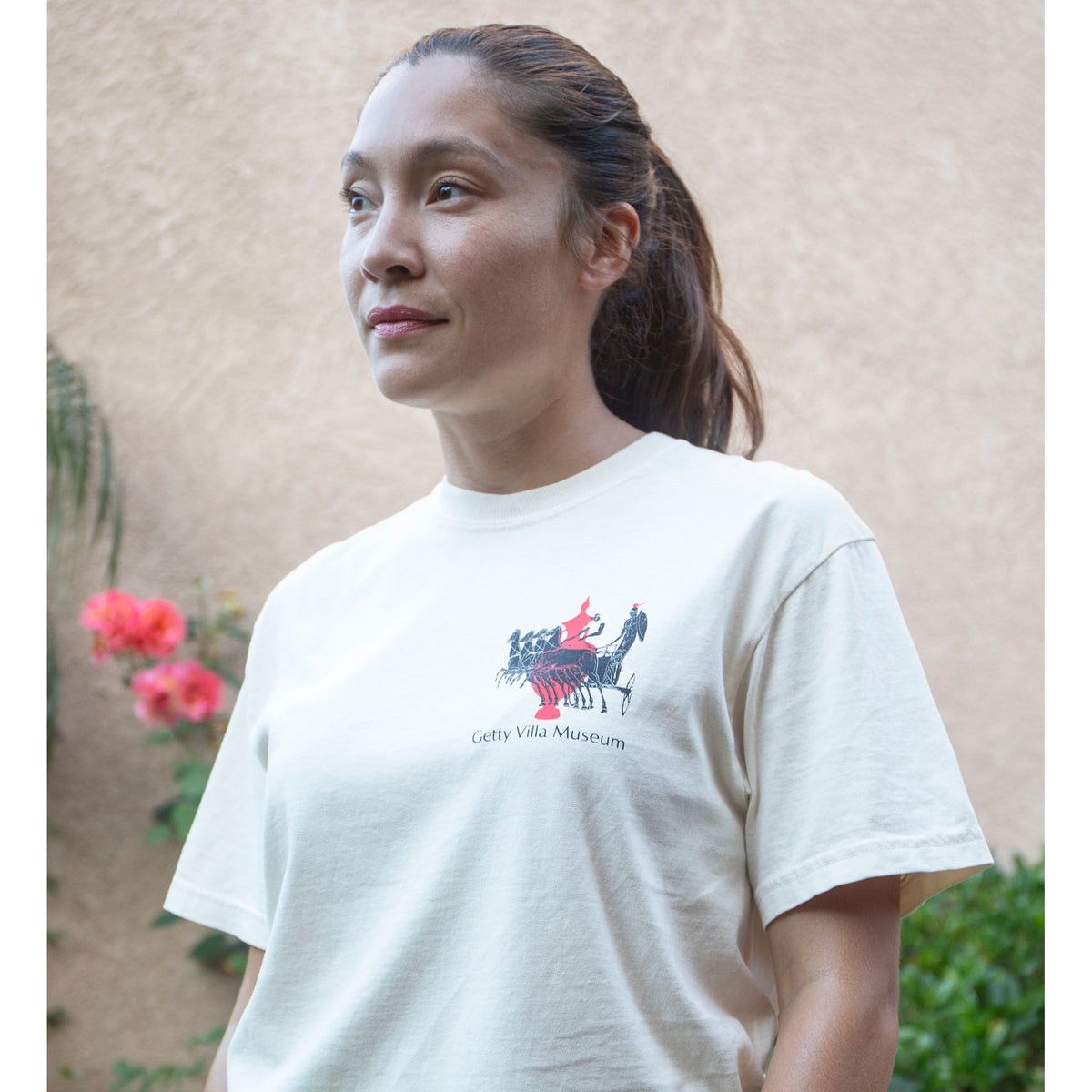 Woman wearing a white t-shirt with a logo and text, standing outdoors.