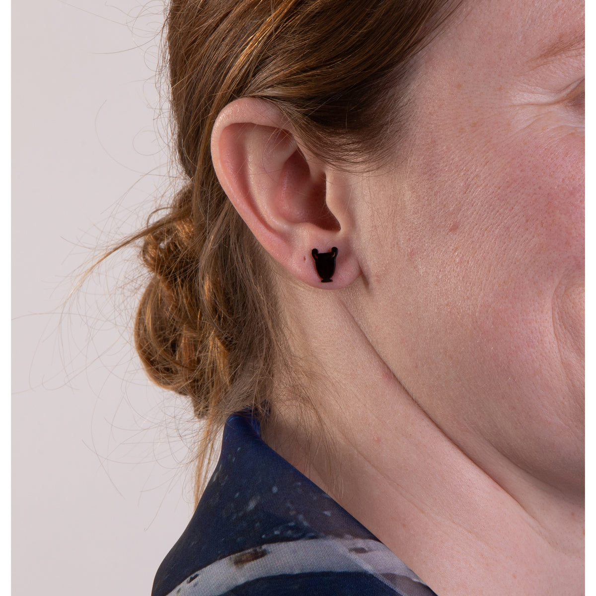 Close-up of an ear with a black vessel-shaped earring on a plain background