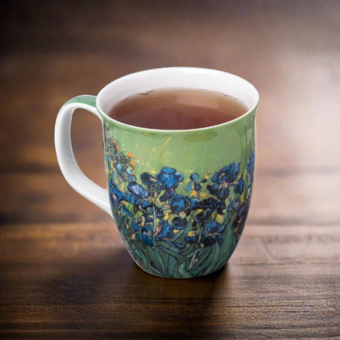 A ceramic mug with a green and blue floral design, filled with tea and placed on a dark wooden table.